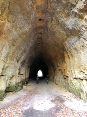 Two hikers walking through the arched sandstone tunnel at Blackhand Gorge toward the far opening