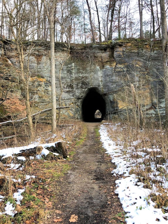A dirt path through light snow leading to the tunnel mouth in a tall sandstone cliff