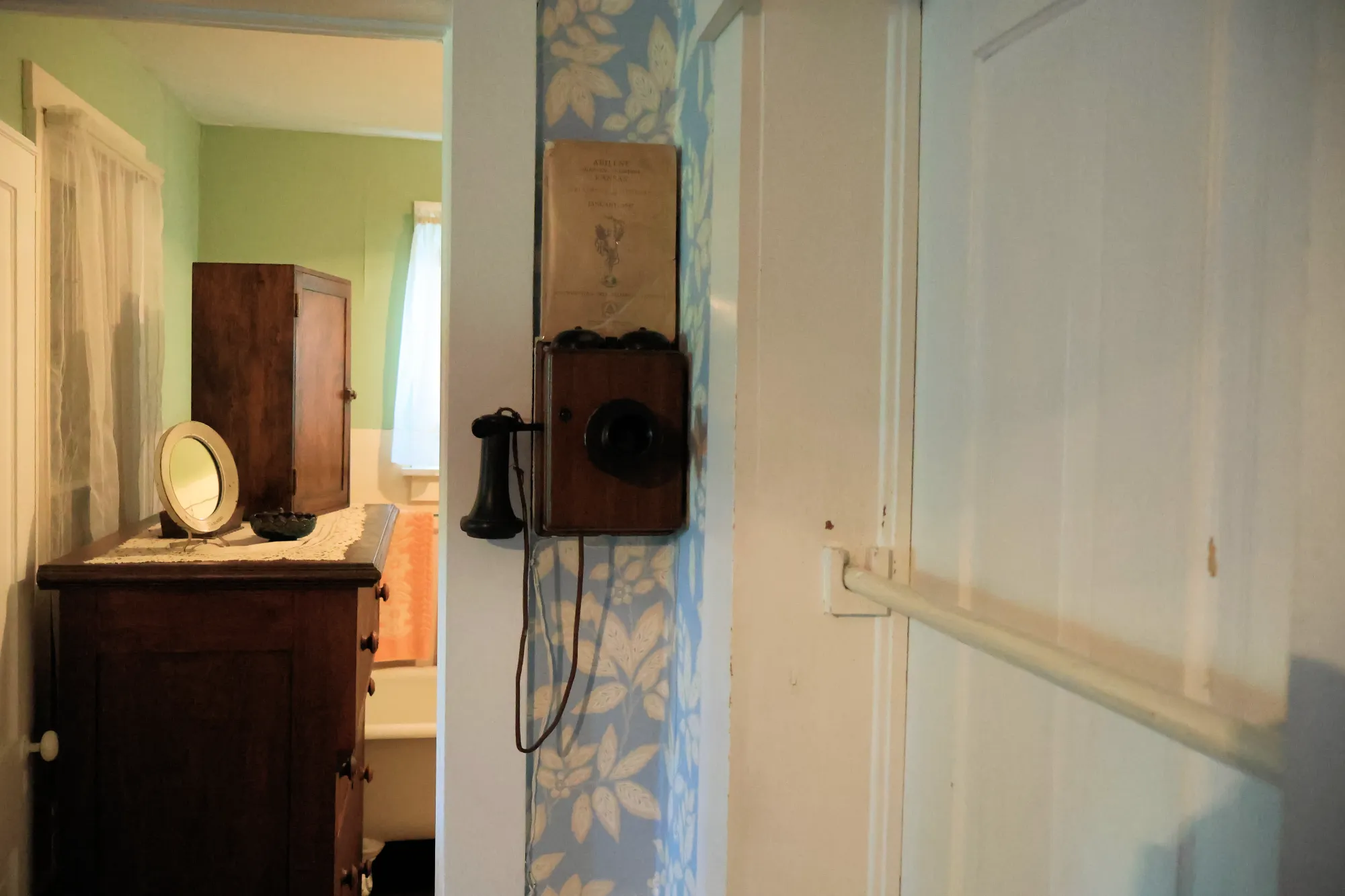 Wall-mounted antique telephone next to a wooden cabinet in a period room