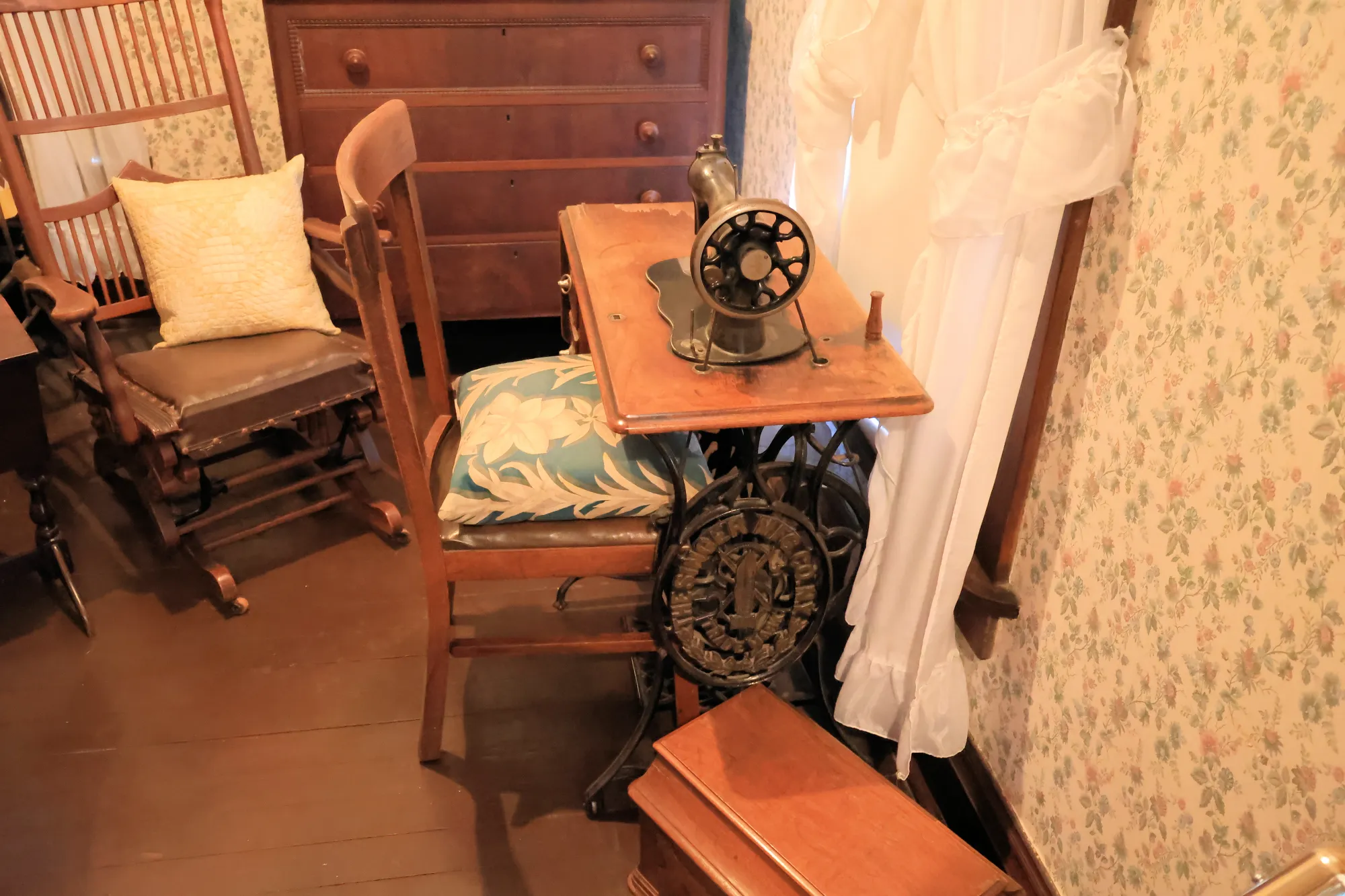 Corner of a historic room with a treadle sewing machine and wooden chairs