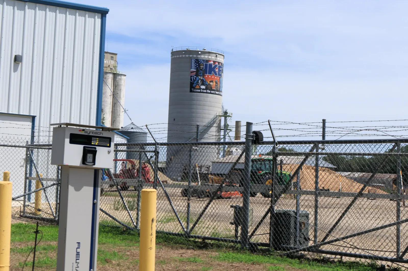 Grain elevators and silos behind a chain-link fence in rural Kansas